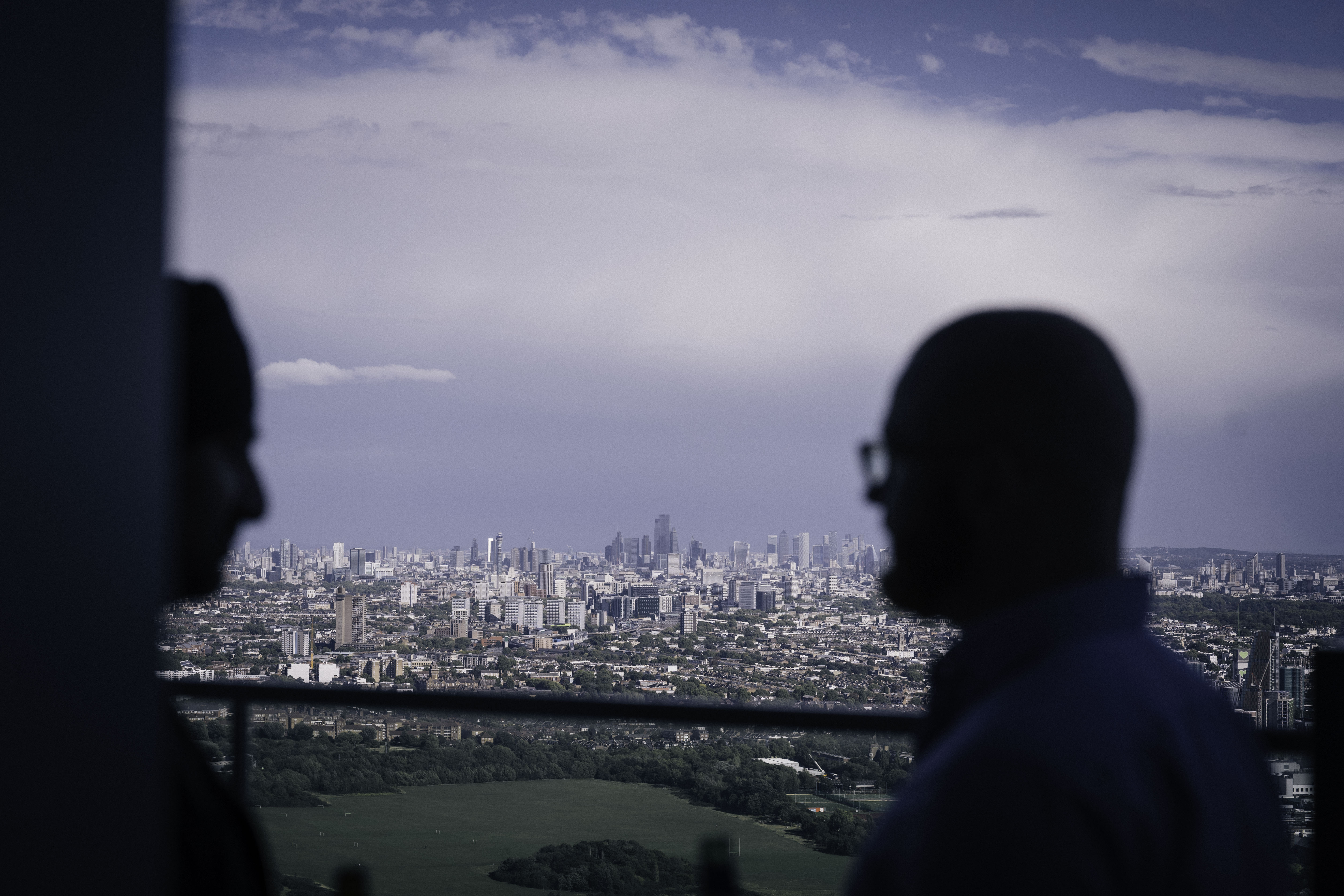 Silhouettes of two people standing on a high-rise balcony overlooking a vast cityscape.