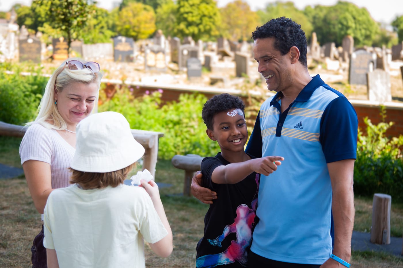 A resident chatting with Flint Housing staff while a face-painted child points and smiles in the communal garden