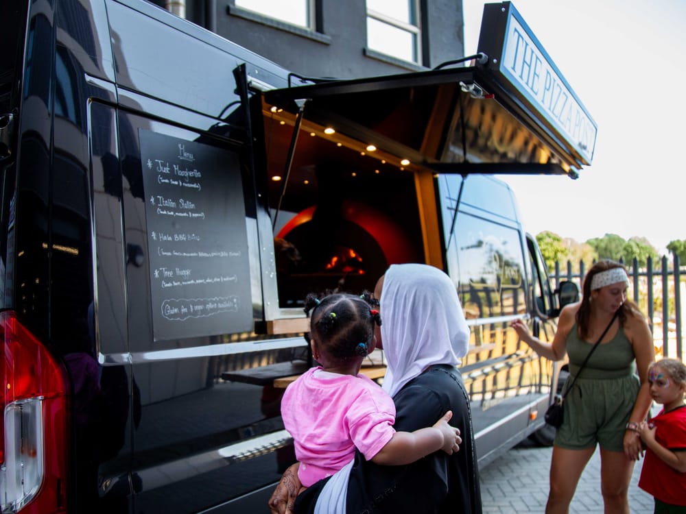 A resident and child reading The Pizza Post chalkboard menu beside the wood-fired oven